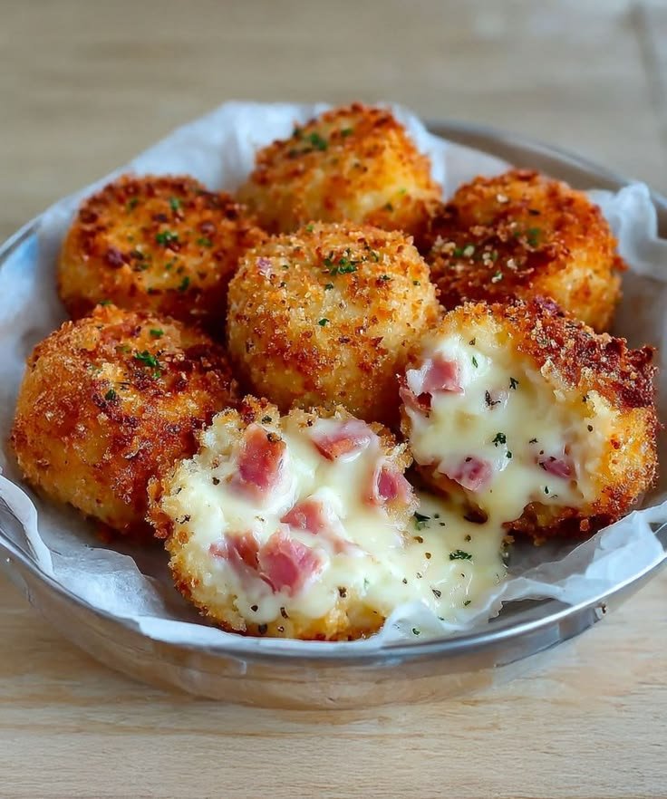 Ración de croquetas de jamón ibérico redondas y súper crujientes en un cuenco metálico, con dos de ellas abiertas mostrando un relleno cremoso de bechamel líquida y trozos de jamón con perejil espolvoreado.